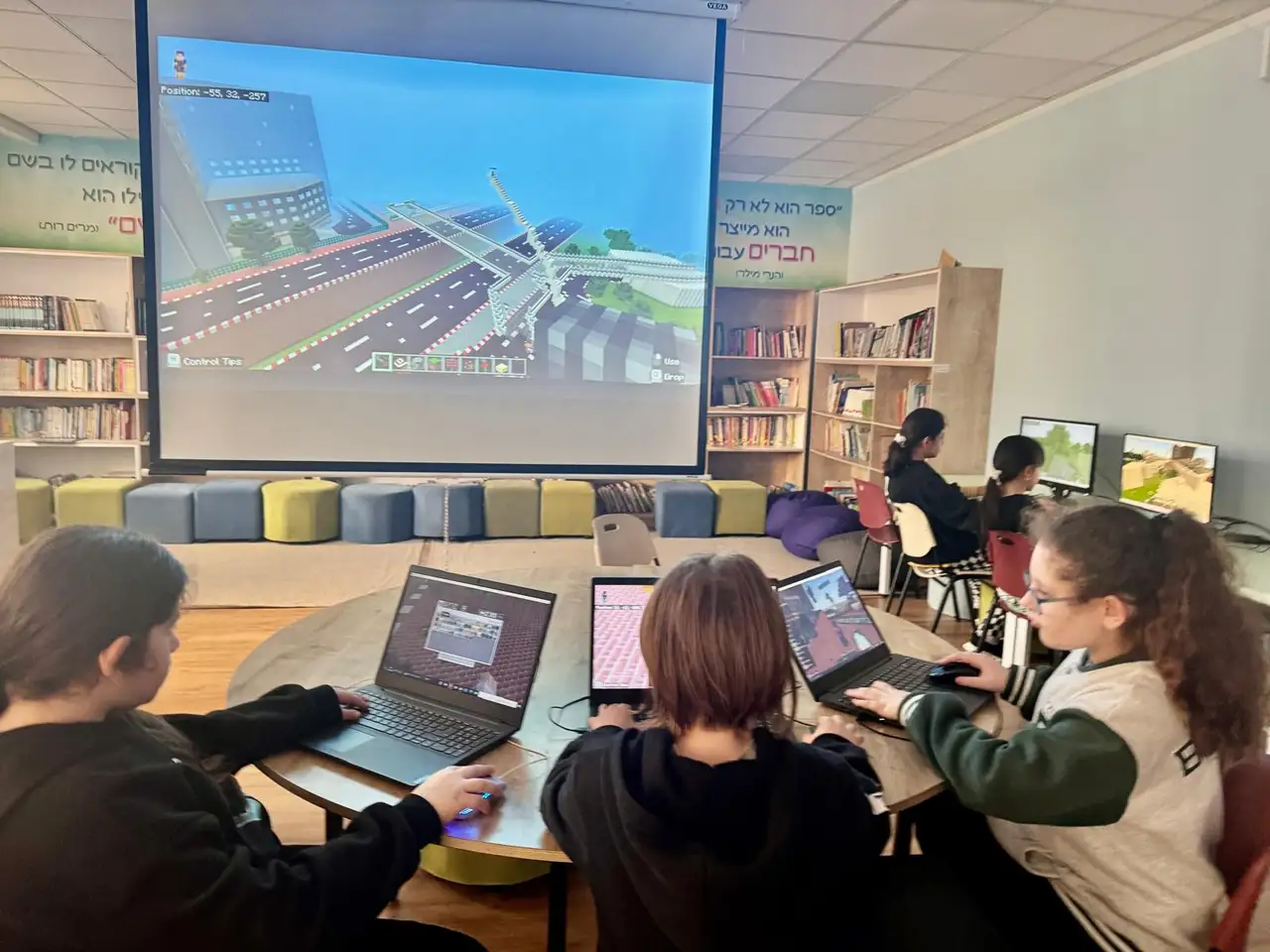 A class building a city in Minecraft on laptops, with their world projected on the big screen